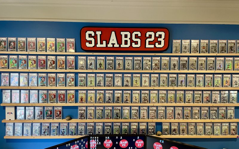 Wall of PSA-graded slabs at the Slabs 23 office beneath the SLABS 23 sign